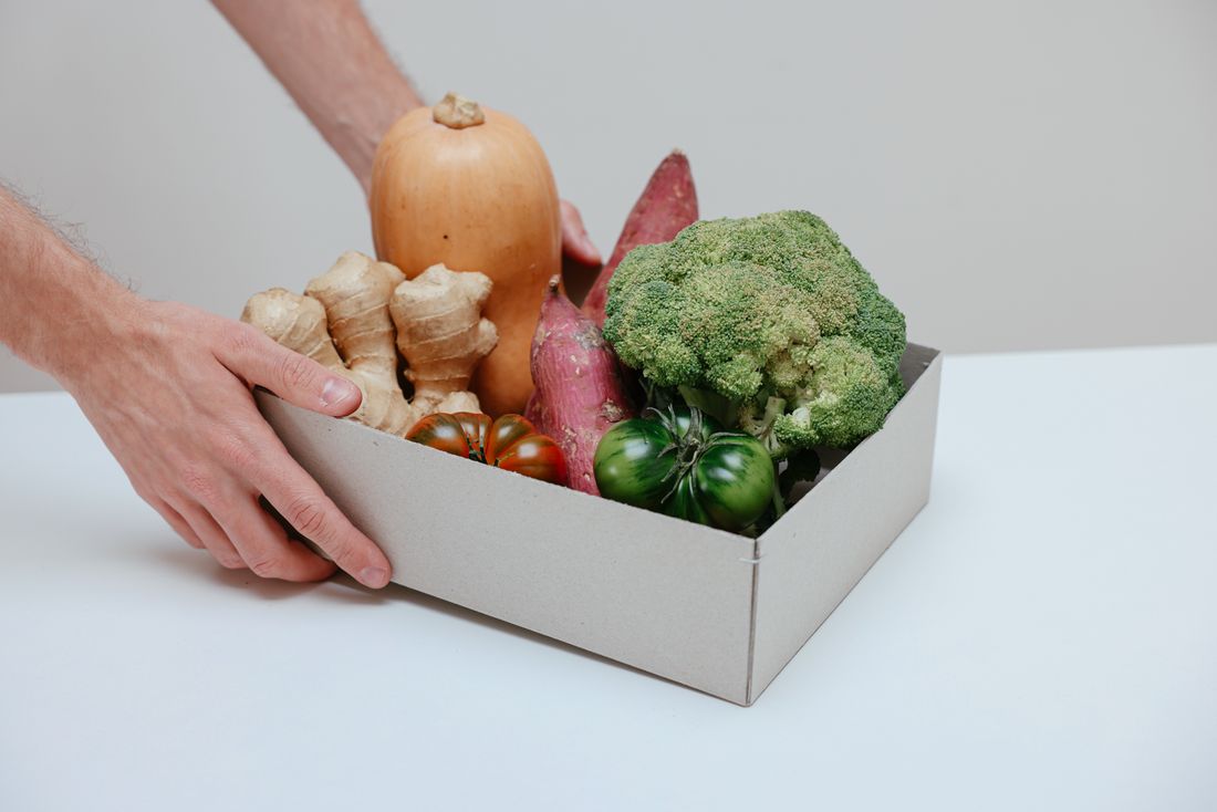 Manos sosteniendo una caja de verduras recién recogidas